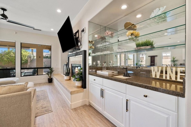 bar with ceiling fan, light hardwood / wood-style floors, sink, white cabinetry, and dark stone counters