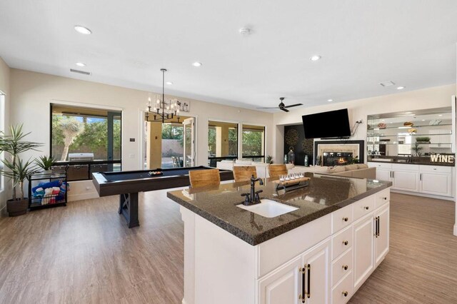 kitchen featuring ceiling fan with notable chandelier, white cabinetry, dark stone counters, sink, and a kitchen island with sink