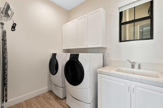 washroom featuring light hardwood / wood-style floors, sink, washing machine and clothes dryer, and cabinets