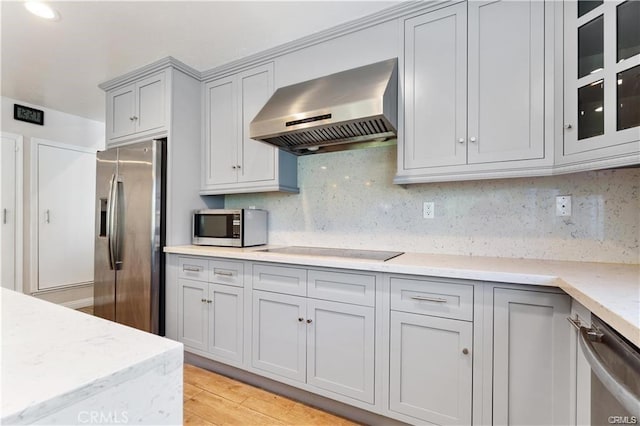 kitchen with light stone countertops, appliances with stainless steel finishes, wall chimney exhaust hood, and tasteful backsplash