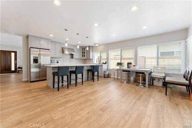 kitchen with pendant lighting, appliances with stainless steel finishes, a kitchen bar, wall chimney range hood, and gray cabinets