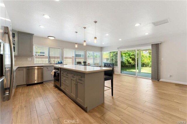 kitchen featuring gray cabinets, appliances with stainless steel finishes, decorative light fixtures, a kitchen breakfast bar, and a center island