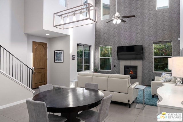 tiled dining area featuring ceiling fan, a high ceiling, plenty of natural light, and a tiled fireplace