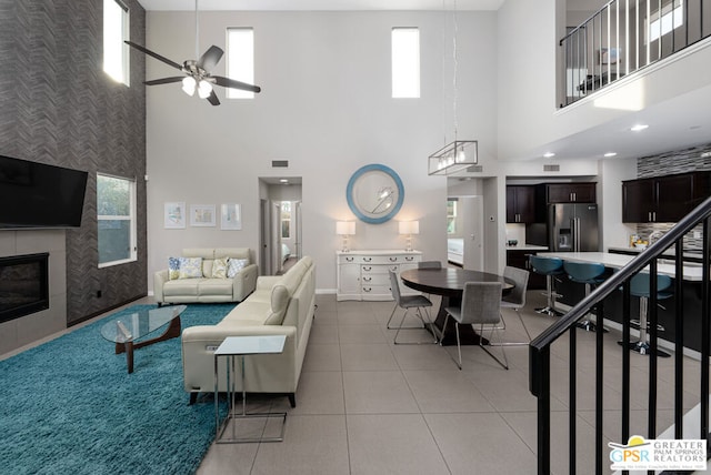 living room featuring ceiling fan, light tile patterned floors, a fireplace, and a high ceiling