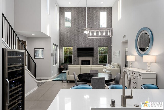 tiled living room with ceiling fan, a healthy amount of sunlight, beverage cooler, and a high ceiling