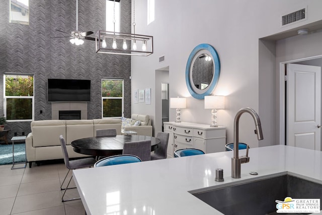 kitchen with ceiling fan, a high ceiling, light tile patterned flooring, a tile fireplace, and sink