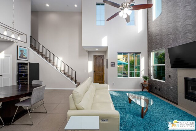 living room with ceiling fan, tile patterned flooring, wine cooler, a towering ceiling, and a tile fireplace