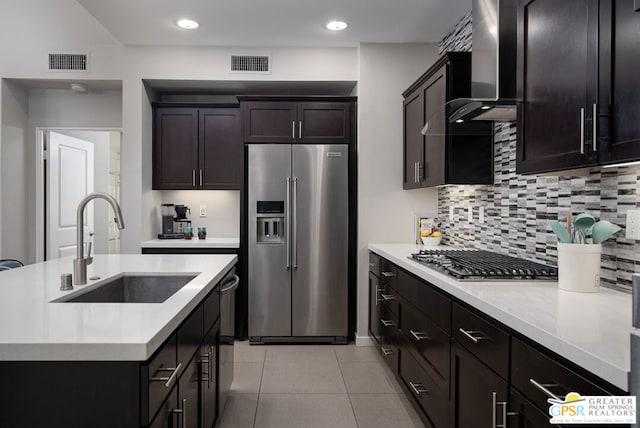 kitchen featuring wall chimney range hood, stainless steel appliances, sink, backsplash, and dark brown cabinets