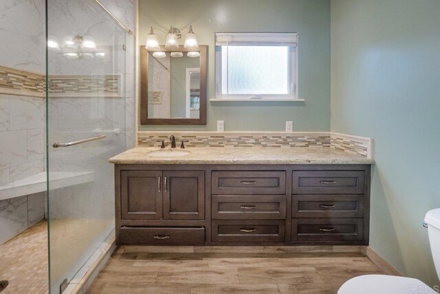 bathroom with toilet, vanity, backsplash, and a tile shower