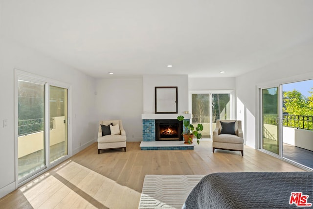 bedroom with access to exterior, a tiled fireplace, and light wood-type flooring