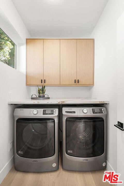 clothes washing area with cabinets, washer and clothes dryer, and light hardwood / wood-style floors