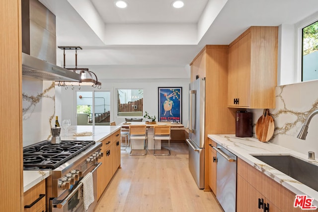 kitchen with high quality appliances, plenty of natural light, sink, and wall chimney range hood