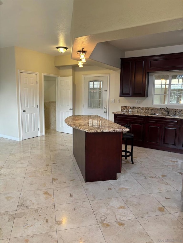 kitchen with a kitchen island, a breakfast bar, sink, dark brown cabinetry, and light stone counters