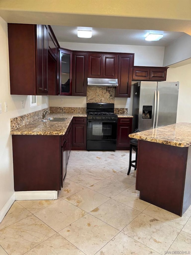 kitchen with black range with gas stovetop, stainless steel fridge, light stone counters, and sink