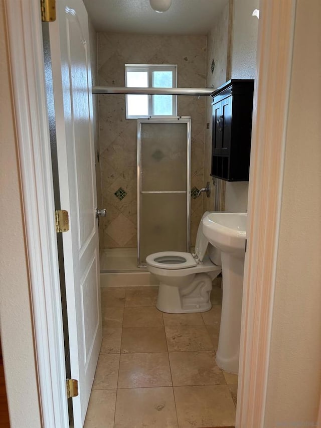 bathroom featuring tile patterned floors, toilet, and a shower with door