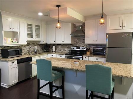 kitchen with light stone countertops, appliances with stainless steel finishes, white cabinets, and wall chimney range hood