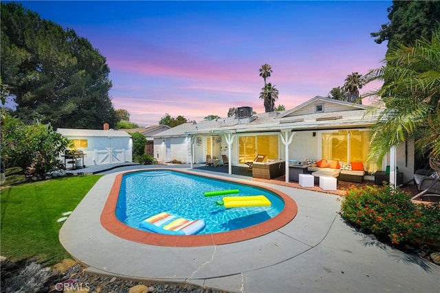 pool at dusk with an outdoor hangout area, a patio area, a shed, and a lawn