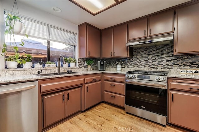 kitchen featuring light stone countertops, stainless steel appliances, tasteful backsplash, sink, and light hardwood / wood-style flooring