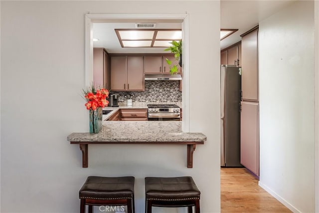 kitchen featuring kitchen peninsula, a breakfast bar area, stainless steel appliances, decorative backsplash, and light hardwood / wood-style flooring