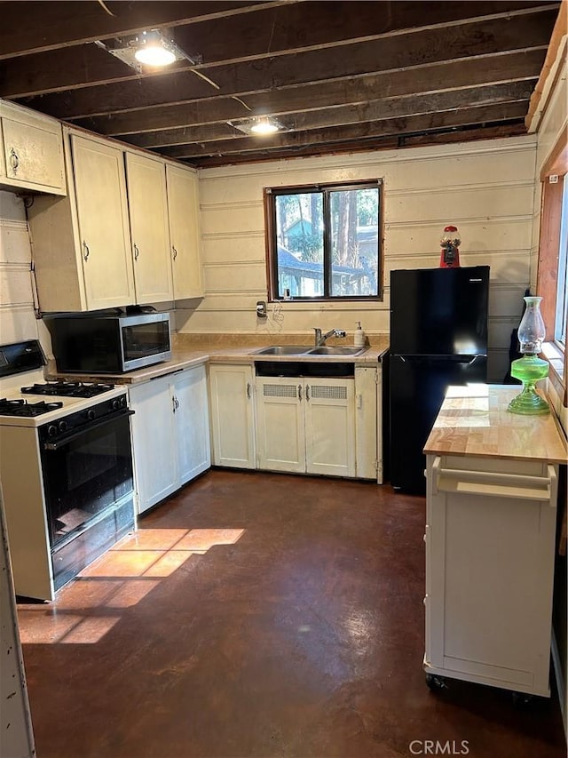 kitchen featuring black fridge, white cabinetry, gas range, and sink