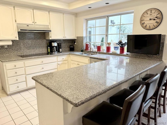 kitchen with black electric cooktop, a kitchen bar, kitchen peninsula, and sink