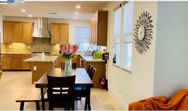 kitchen with wall chimney exhaust hood, a kitchen island, tasteful backsplash, sink, and light stone counters