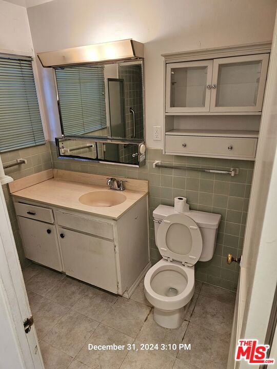 bathroom with toilet, vanity, tile walls, and tile patterned floors