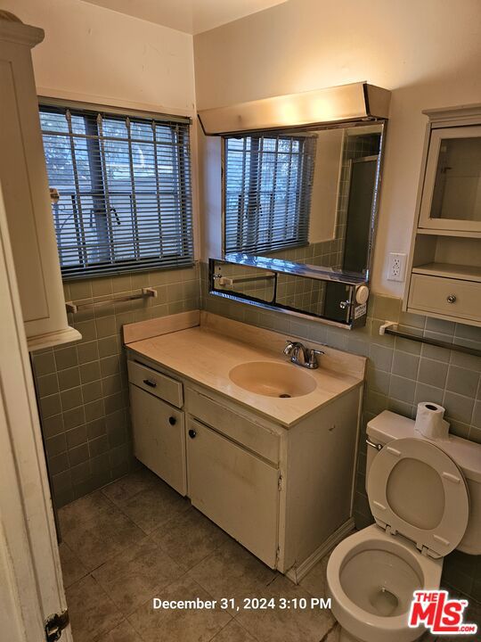 bathroom with toilet, tile walls, tile patterned floors, and vanity