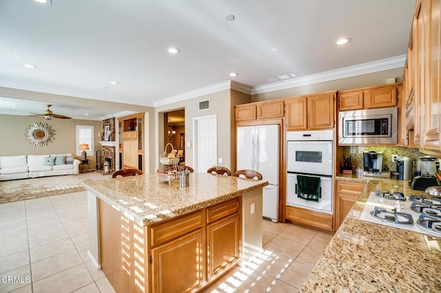 kitchen with crown molding, light stone countertops, light tile patterned flooring, white appliances, and a kitchen island