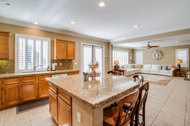 kitchen with a center island, crown molding, sink, ceiling fan, and light stone counters