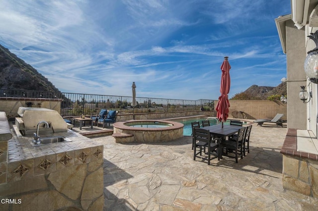 view of patio with area for grilling, sink, a mountain view, and a pool with hot tub