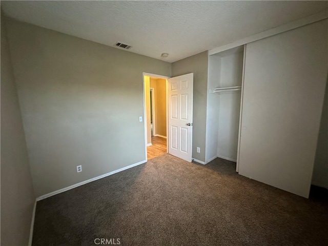 unfurnished bedroom featuring a textured ceiling, a closet, and dark carpet