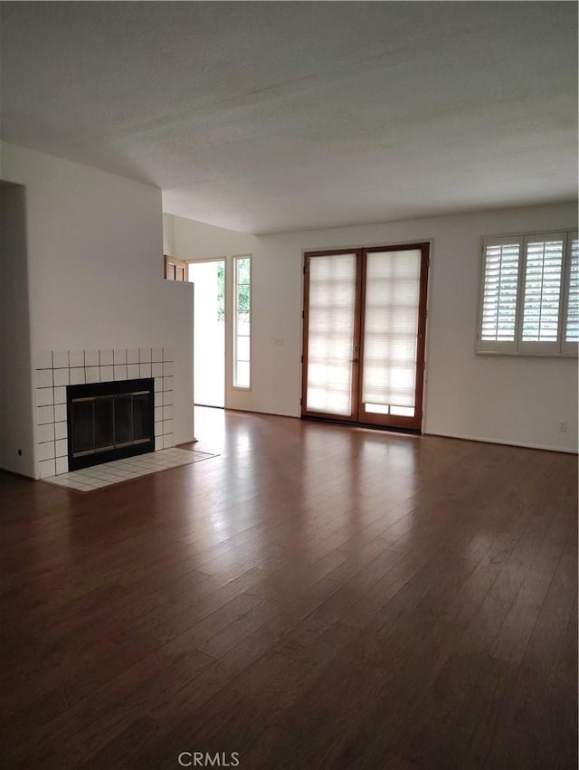 unfurnished living room featuring wood-type flooring, a tile fireplace, and a healthy amount of sunlight