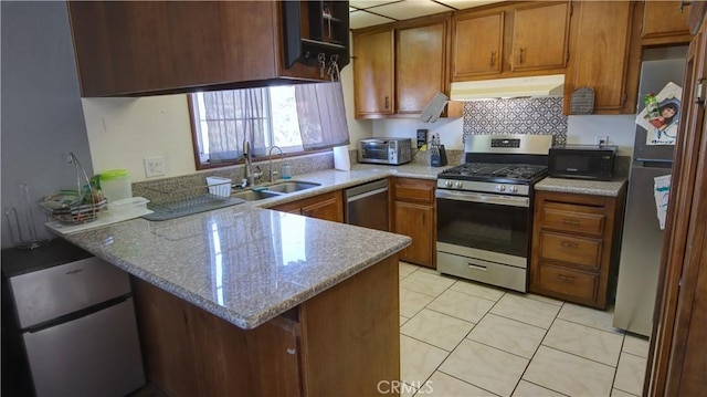 kitchen with light stone countertops, stainless steel appliances, sink, kitchen peninsula, and light tile patterned flooring