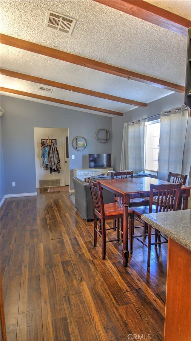 dining room with dark wood-type flooring, a textured ceiling, and beam ceiling