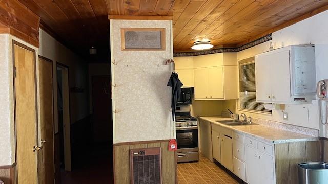 kitchen with wood walls, sink, stainless steel range, wood ceiling, and white cabinets