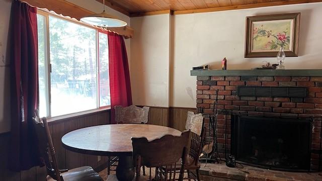 dining room featuring wooden ceiling, wood walls, and a brick fireplace