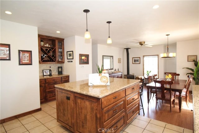 kitchen with ceiling fan, a kitchen island, light tile patterned flooring, hanging light fixtures, and a wood stove