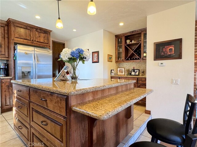 kitchen with pendant lighting, a kitchen island, a kitchen bar, stainless steel fridge, and light tile patterned flooring