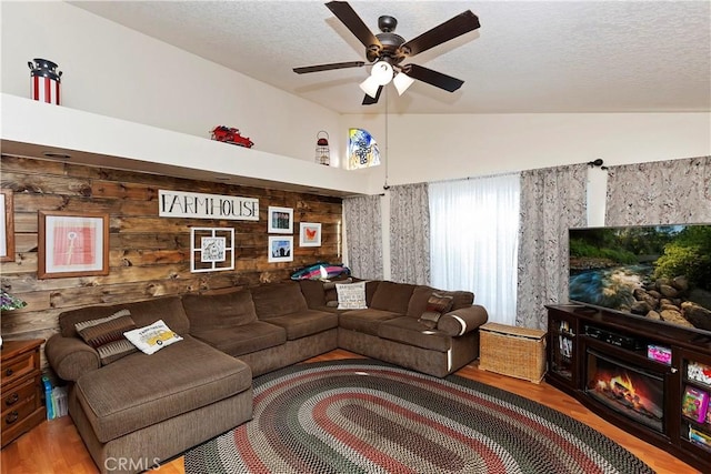 living room featuring ceiling fan, a fireplace, wood walls, wood-type flooring, and a textured ceiling