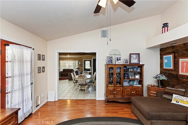 living room featuring ceiling fan, a textured ceiling, light hardwood / wood-style flooring, and lofted ceiling