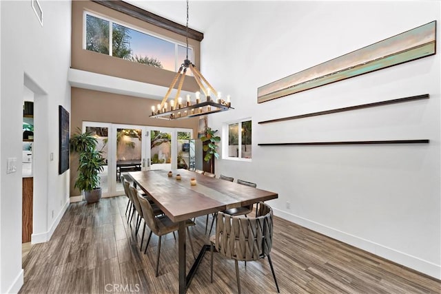 dining room with french doors, an inviting chandelier, a towering ceiling, and hardwood / wood-style flooring