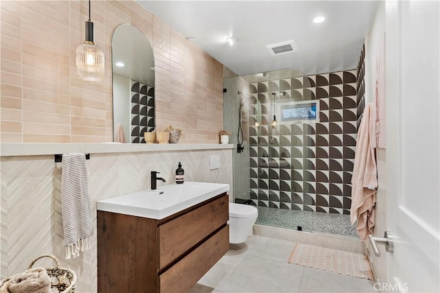 bathroom featuring toilet, vanity, tile walls, tile patterned flooring, and a tile shower