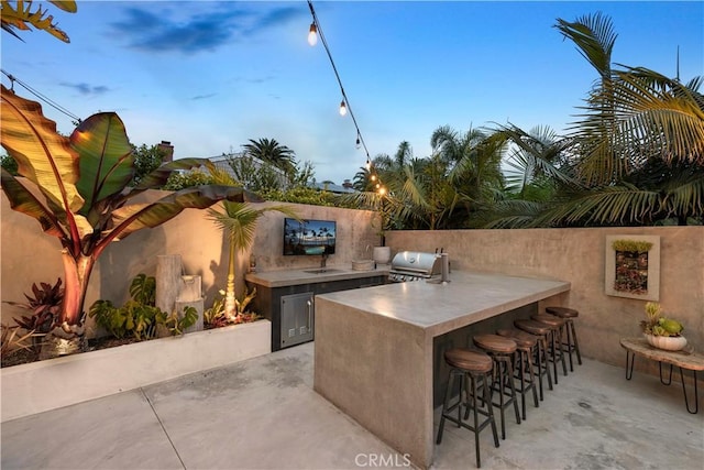 patio terrace at dusk featuring grilling area, a bar, and exterior kitchen