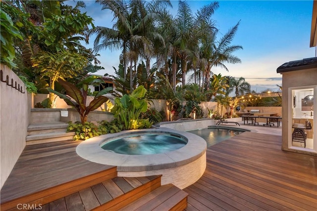 pool at dusk with an in ground hot tub and a deck