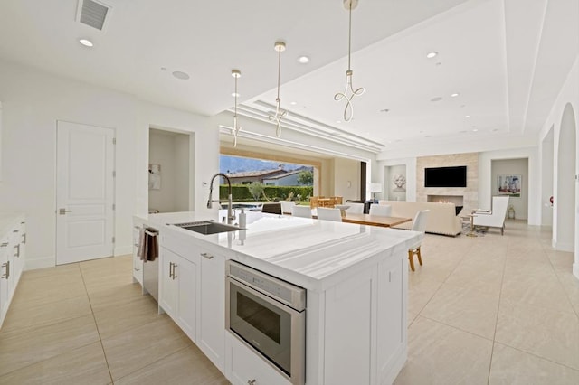 kitchen featuring white cabinetry, an island with sink, decorative light fixtures, light tile patterned flooring, and sink