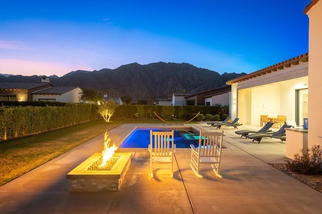 pool at dusk with a mountain view, an outdoor fire pit, and a patio