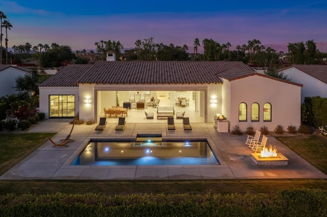 back house at dusk with a pool with hot tub, an outdoor fire pit, and a patio area