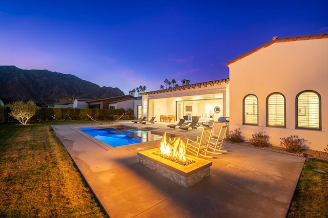 pool at dusk with an outdoor living space with a fire pit, a mountain view, and a patio