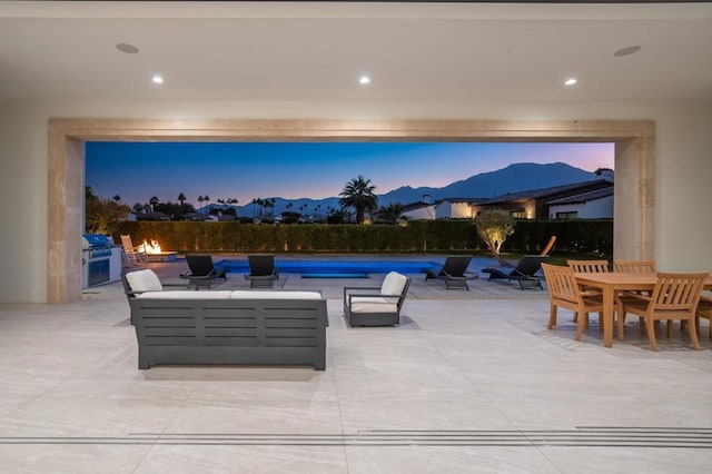 patio terrace at dusk featuring a grill, outdoor lounge area, exterior kitchen, a mountain view, and a swimming pool